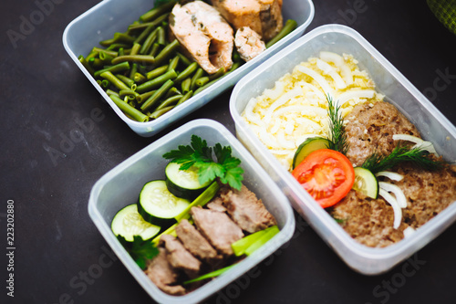 the healthy food in the containers on black background: snack, dinner, lunch. Baked fish, beans, beef cutlets, mashed potatoes, meat and vegetables tomatoes, cucumbers.