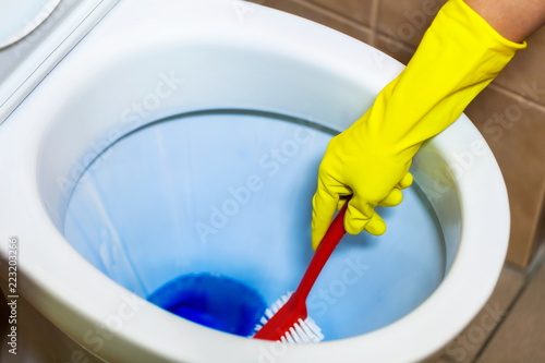 Hand with brush cleans toilet bowl