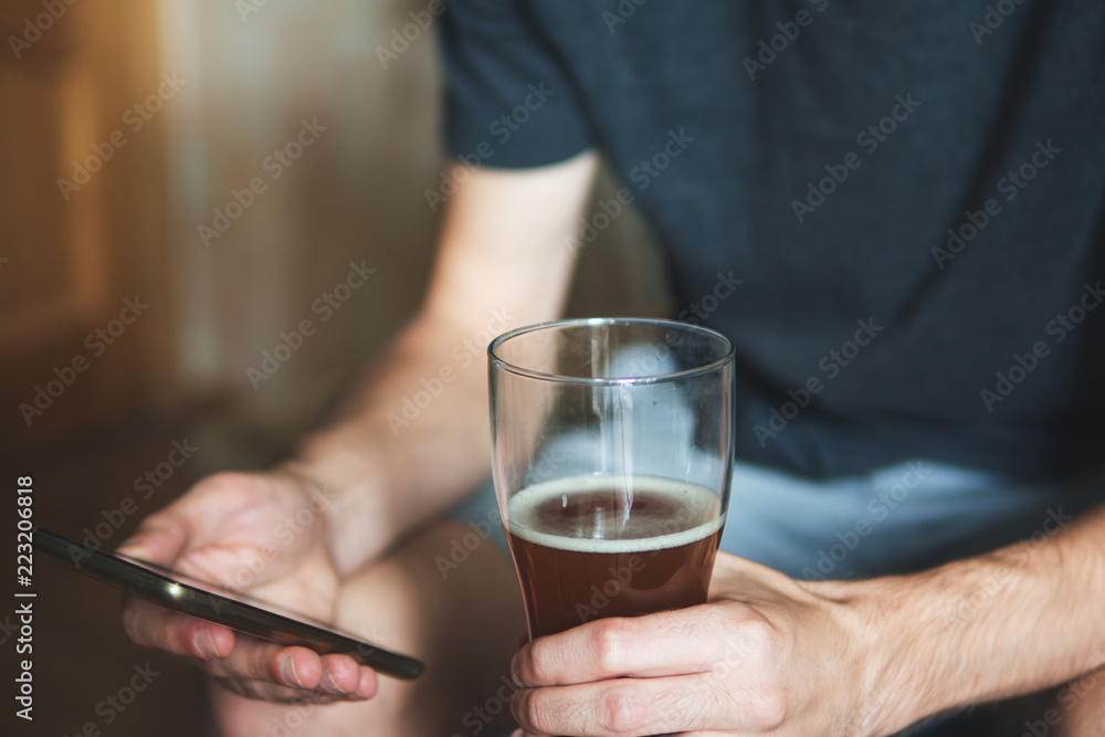 Partial view of a person with alcohol and a phone. Drinks and rests at home Partial view of a person with alcohol and a phone. Drinks and rests at home