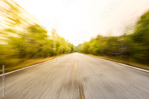 Photograph of asphalt road a long the forest, shot in blurred exposed lens zoom.