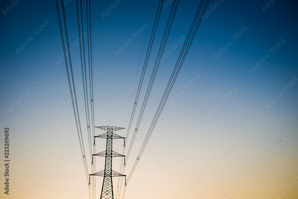 High voltage power tower close up on the worm tone sky before sunset.