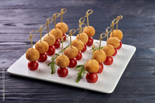 Appetizing and unusual snack for the festive table. A small treat on a skewer. A tiny round cutlet in breadcrumbs and a cherry tomato. Vegetarian snack with potato ball and tomato.
