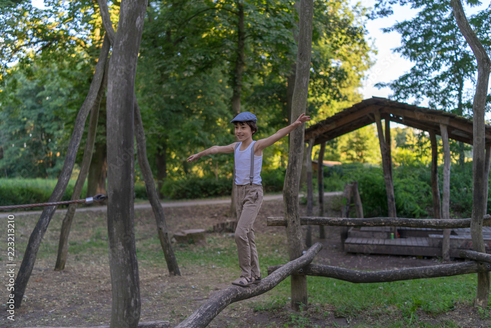 A boy dressed in pants with suspenders and a sleeveless shirt in the playground.