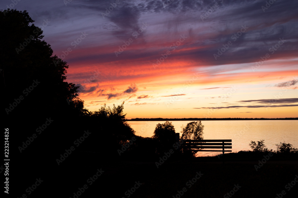 Fototapeta premium Sunset silhouette with bench and shoreline