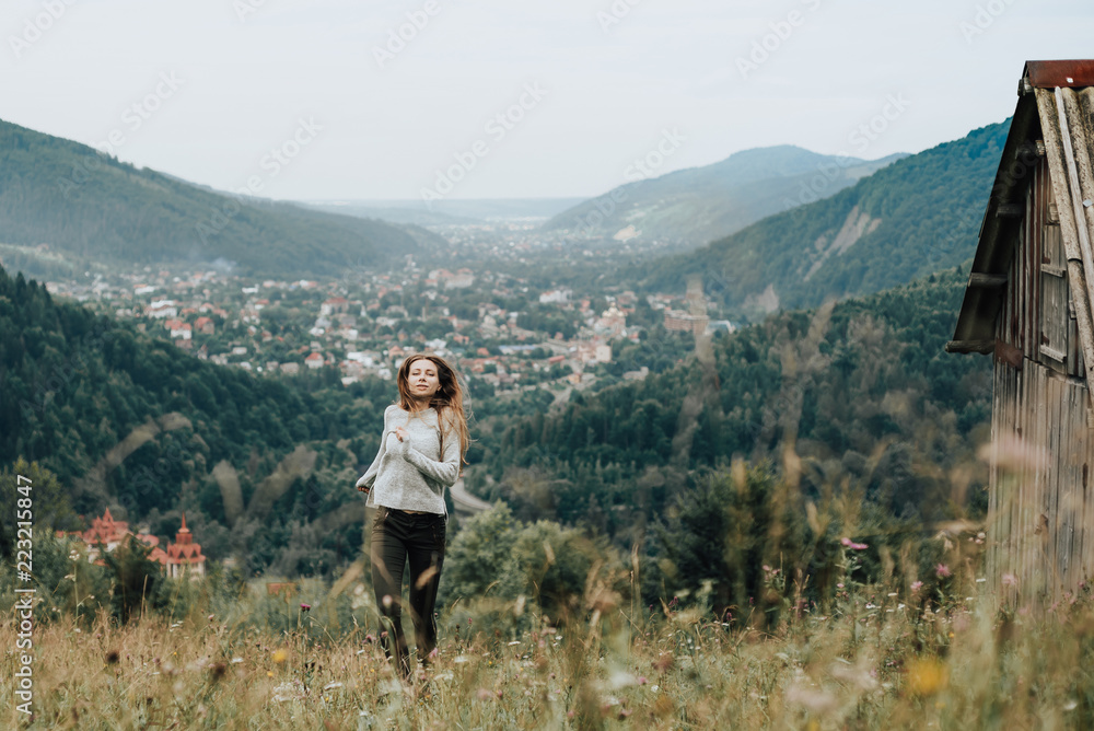 Playful young girl looking and smiling while jumping on a lawn in the mountains