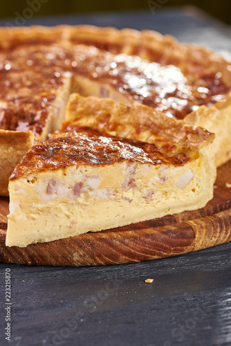 Appetizing cheese cake with sausage, ham. Snack unsweetened cake with crispy cheese crust. An unusual variant of pizza is "four cheeses". The pie lies on a round wooden cutting board.