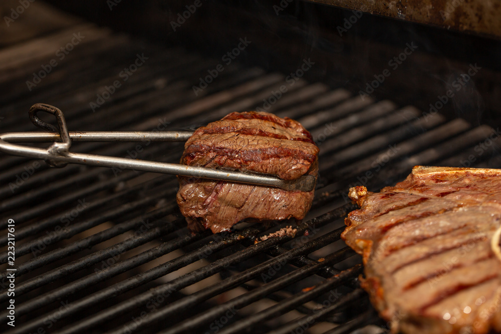 Tongs Holding Grilled Pork Ribs. Hot Flaming BBQ Grill on the Background Tongs Holding Grilled Pork Ribs. Hot Flaming BBQ Grill on the Background