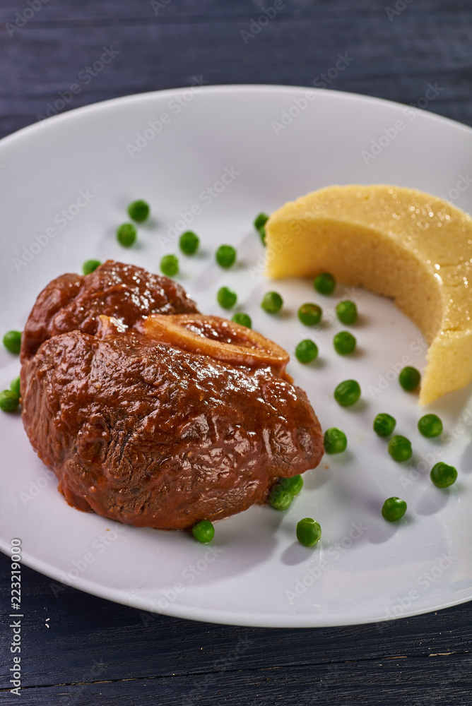 Unusual serving of food in a cafe, restaurant. Potato puree / polenta in the form of an incomplete moon, green peas in the form of stars in the sky. A large piece of appetizing meat on the bone.