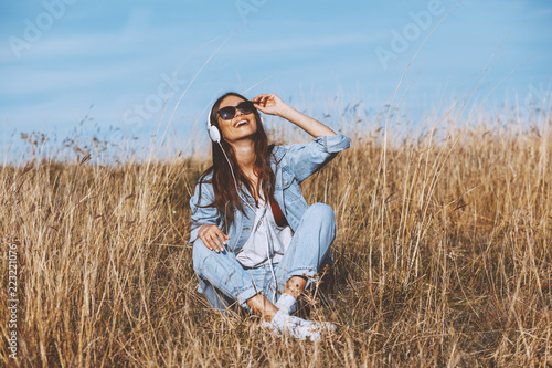 Young woman listens to music and sitting  in the meadow