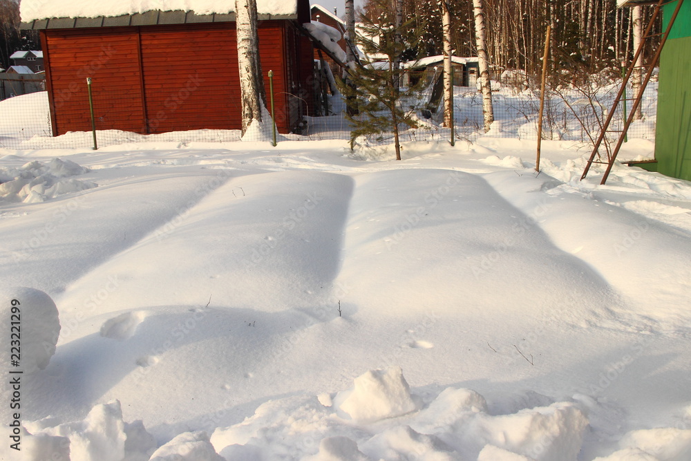 Beds in the garden in the country in the winter under the snow on the background of a wooden brown barn Beds in the garden in the country in the winter under the snow on the background of a wooden brown barn