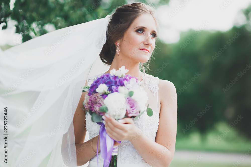 Beautiful bride in elegant white dress holding bouquet posing in park Beautiful bride in elegant white dress holding bouquet posing in park