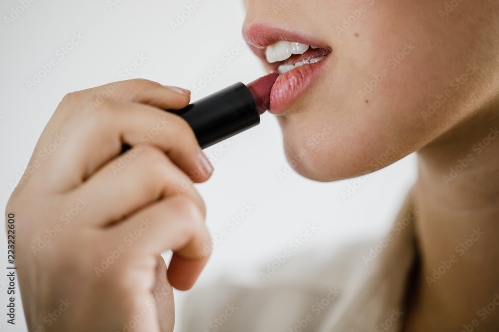 Junge Frau schminkt sich die Lippen vor einer weißen Wand mit einem Lippenstift