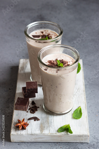 Delicious chocolate drink (milkshake, cocktail or smoothie) in glasses with pieces of chocolate on grey concrete background.