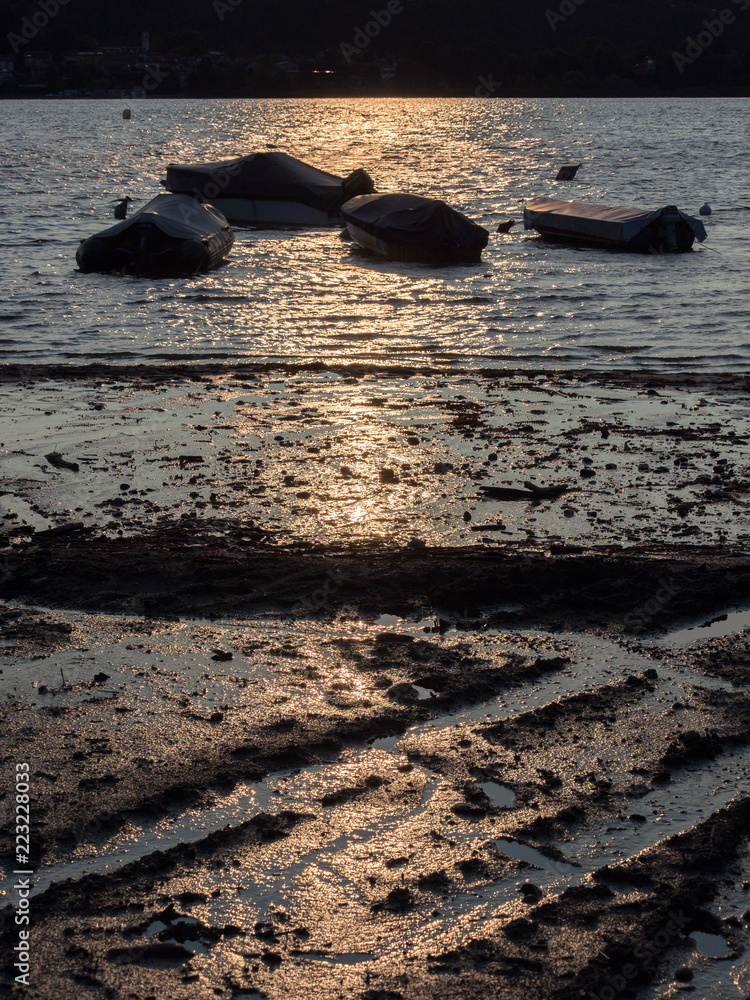 Boote als Silhouetten am Ufer des Lago Maggiore mit Radspuren in der tiefstehenden Sonne, Italien Boote als Silhouetten am Ufer des Lago Maggiore mit Radspuren in der tiefstehenden Sonne, Italien