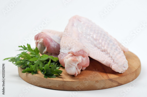 Two wings of turkey on a round wooden board. On the board next to the turkey lies the green of parsley. White background. Close-up.