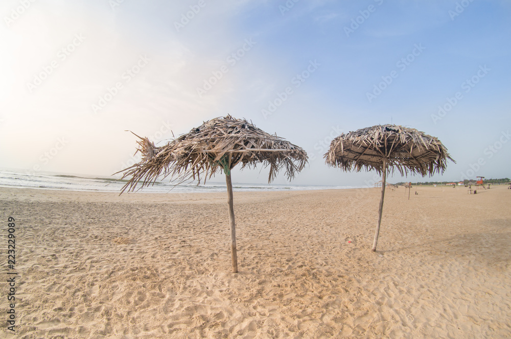 Thatch umbrellas of straw for shade on paradise beach in pondicherry chennai with brown sand, blue skies and the orange from sunrise making this the perfect vacation shot Thatch umbrellas of straw for shade on paradise beach in pondicherry chennai with brown sand, blue skies and the orange from sunrise making this the perfect vacation shot