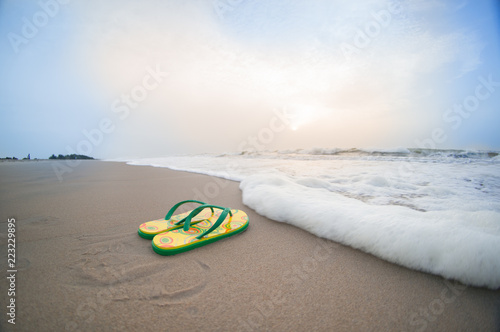 yellow colorful flip flops lying on beach in pondicherry chennai tamil nadu with brown sand, surf, waves and cloudy skies. Perfect vacation shot to relax, unwind and de stress on a working day photo