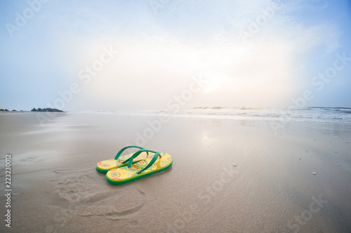 yellow colorful flip flops lying on beach in pondicherry chennai tamil nadu with brown sand, surf, waves and cloudy skies. Perfect vacation shot to relax, unwind and de stress on a working day