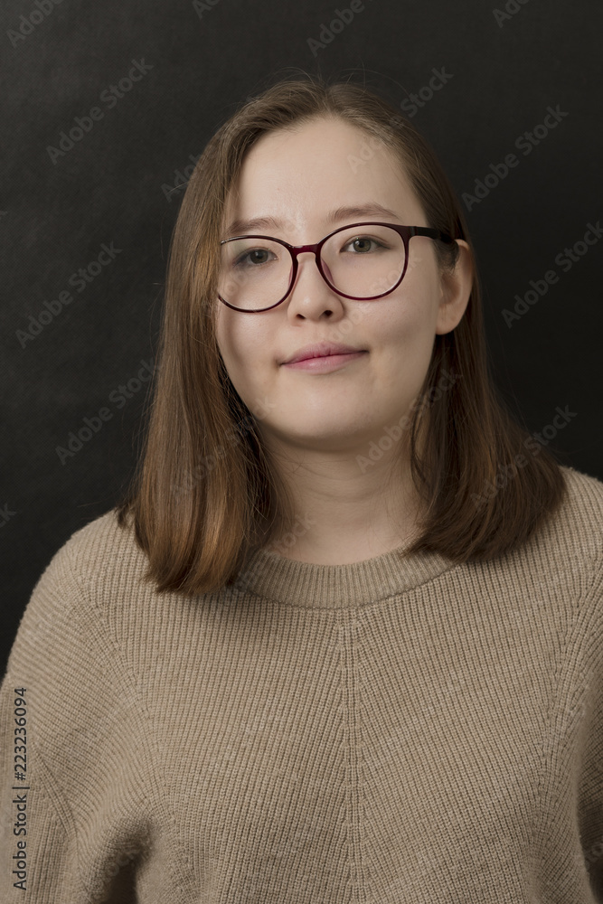 Indoor portrait of graceful smiling Mongolian girl with glasses on black background. Friendly person concept. Young student with a woolen jumper. Indoor portrait of graceful smiling Mongolian girl with glasses on black background. Friendly person concept. Young student with a woolen jumper.