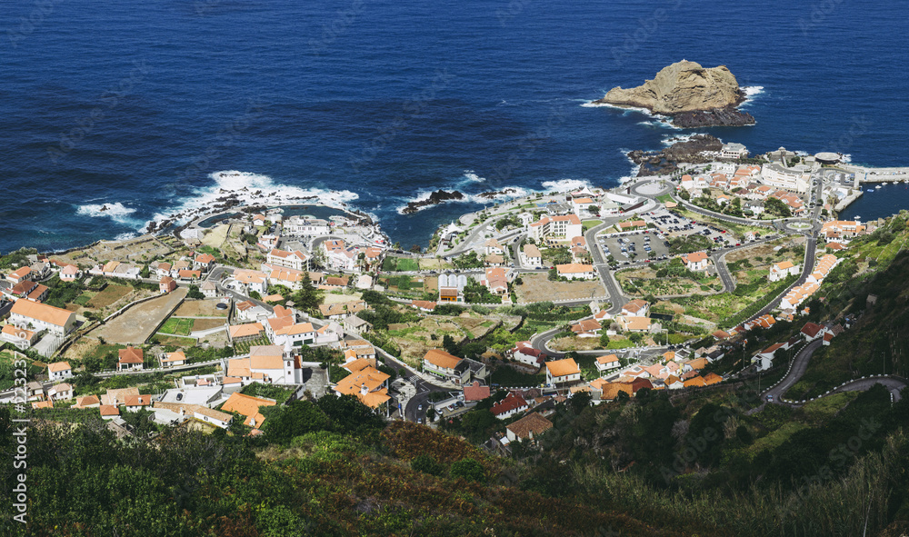 Aerial panoramic view of small town Porto Moniz on Madeira island, Portugal.   Natural outdoor volcanic lava rock pools, ocean, coast, red rooftops, summer.
