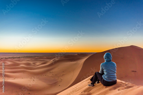 View on woman enjoing sunrise in the Sahara desert next to M'hamid in Morocco