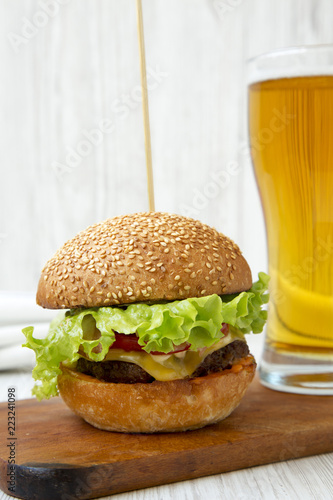 Cheeseburger and glass of beer on wooden board on white wooden surface, side view. Close-up.