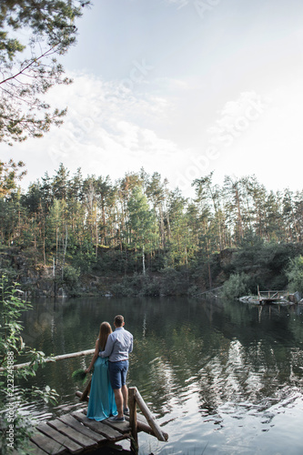 A pair of lovers on a bridge near a lake in a pine forest looking at the water surface