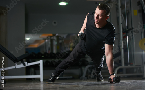 Man doing push-up exercise with dumbbell. Workout Exercise. Sporty Athletic Male Exercising in a gym room 