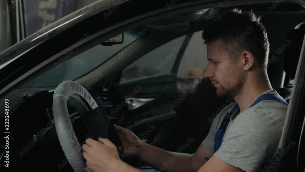 handsome mechanic in uniform is working in auto service. Car repair and maintenance. Performing engine diagnostics with tablet pc laptop handsome mechanic in uniform is working in auto service. Car repair and maintenance. Performing engine diagnostics with tablet pc laptop