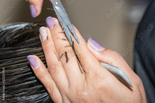Closeup macro shot image of hairstylist hairdresser cutting customer woman hair in salon with scissors and comb  look from behind back side