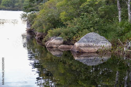 Rocks reflecting in water at shoreline, overcast day, Lewis Lake, Canada, no people.