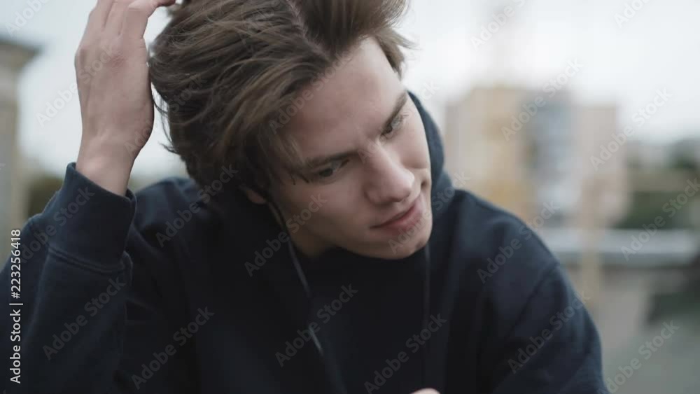 Sad man uses smartphone and earphones on a street roof Sad man uses smartphone and earphones on a street roof