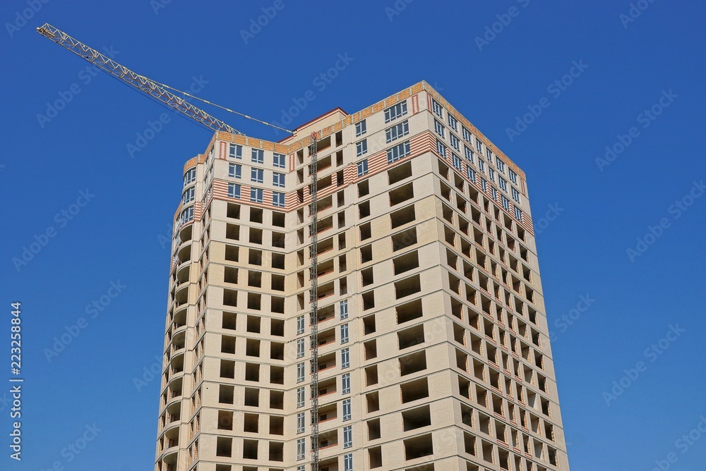 large unfinished gray brown house with windows and a tower crane