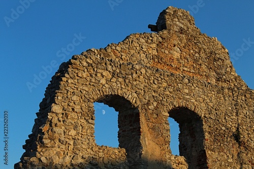 Detail of eastern wall of early gothic part of castle Topolcany during autumn sunset, moon is visible through window on the left. 