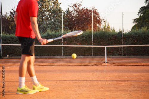 Defocused professional man tennis player playing on the court in the afternoon and bouncing the ball against the ground with the racket.  © pablobenii