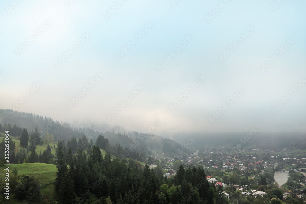 Picturesque landscape with small village and mountain forest covered in mist