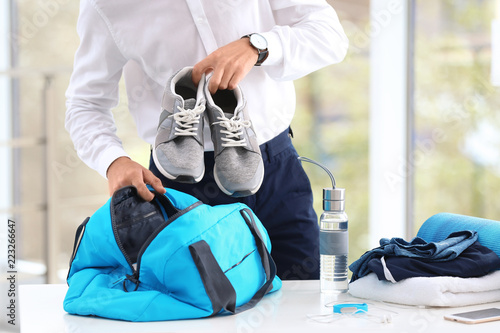 Young businessman packing sports stuff for training into bag in office