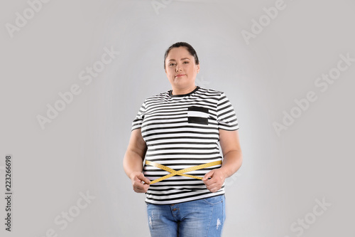 Fat woman with measuring tape on grey background. Weight loss