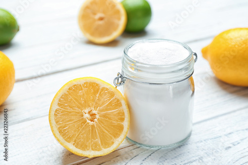 Jar with baking soda and lemon on white wooden table