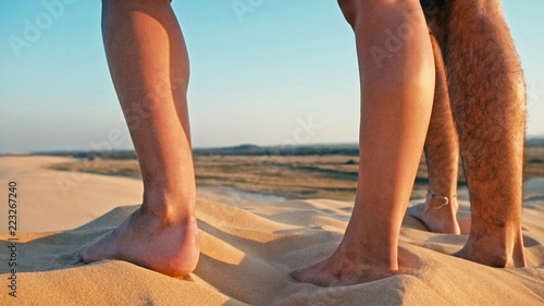closeup of the legs of a young woman and man enjoying the sunset on the peak of one of the desert sand dune