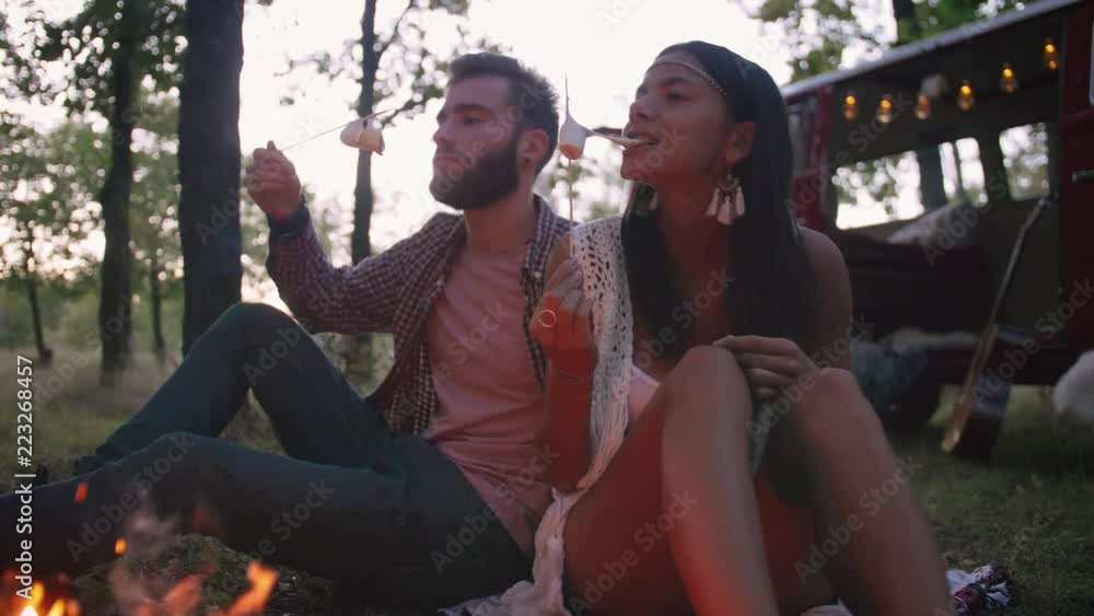 Beautiful young couple roasting marshmallows over a campfire while enjoying their road travel Beautiful young couple roasting marshmallows over a campfire while enjoying their road travel