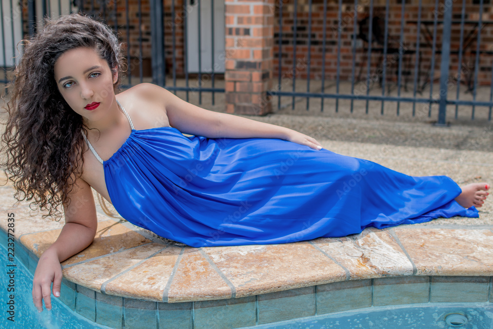 A Beautiful Tan Brunette Woman Lays In A Radiant Colored Blue Dress