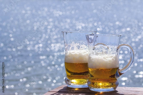 Two mugs of fresh beer on the table against the sea