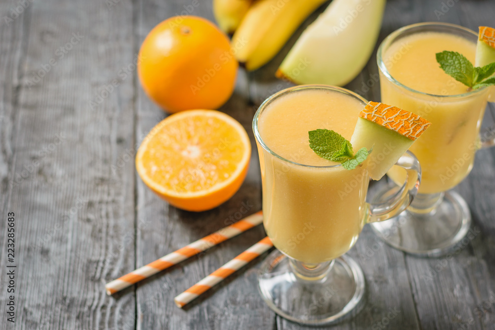 Two glass mugs with melon smoothie, orange and melon on a black wooden table. Two glass mugs with melon smoothie, orange and melon on a black wooden table.