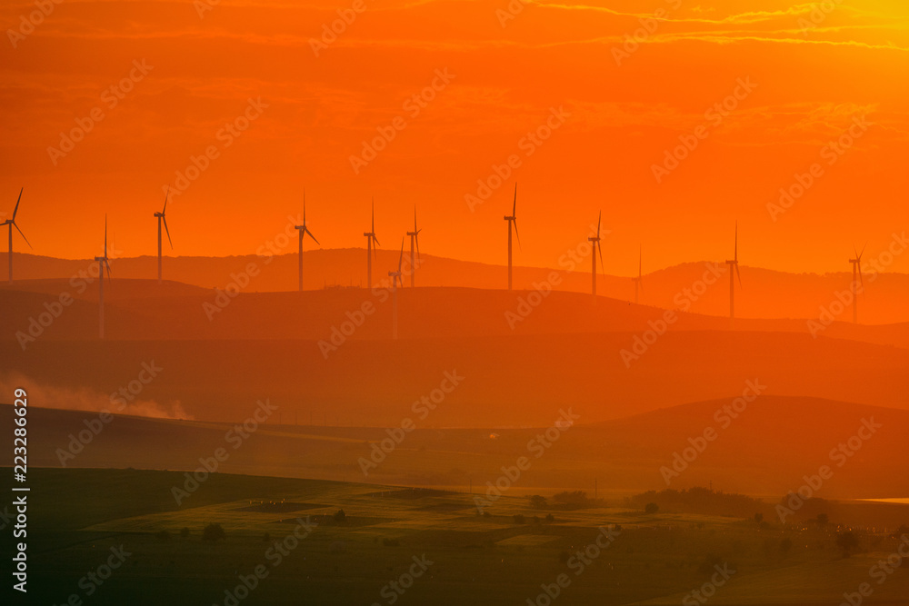 Aeolian turbines placed on hills used to produce ecological green electricity shot at sunset with a field in the foreground