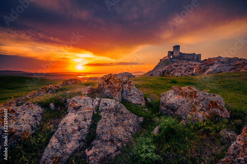 Old ruined citadel on a rocky hill shot at sunset with some rocks in the foreground
