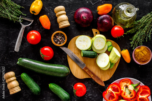 Cooking vegetable stew concept. Fresh vegetables squash, bell pepper, tomato, spices and cutting doard on black background top view photo