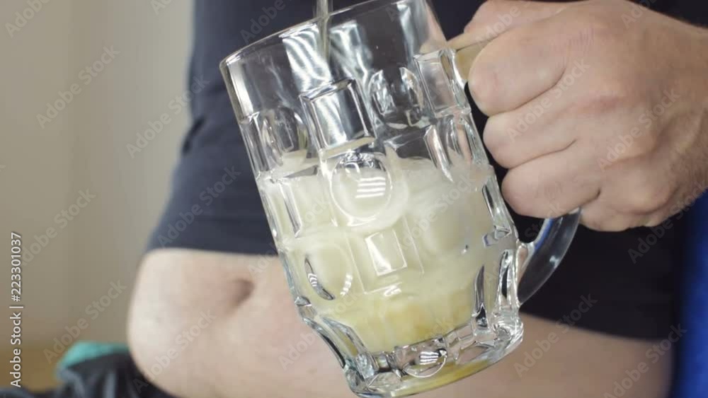 The fat man pours beer into a glass. Beer belly from harmful food. Bad food, gluttony. Closeup