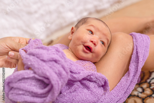 Mother cleaning her little baby and wrapping with purple blanket on her lap. Cut baby gilr samiling, good mood. photo