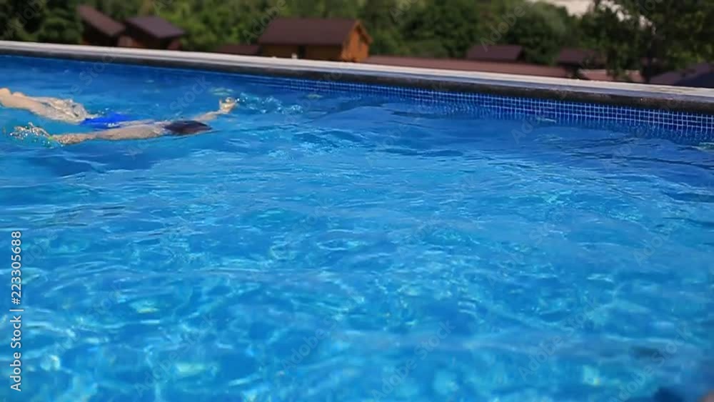 a young beautiful woman with red hair and a blue swimsuit swimming in a luxury outdoor pool on a Sunny summer day. a young beautiful woman with red hair and a blue swimsuit swimming in a luxury outdoor pool on a Sunny summer day.